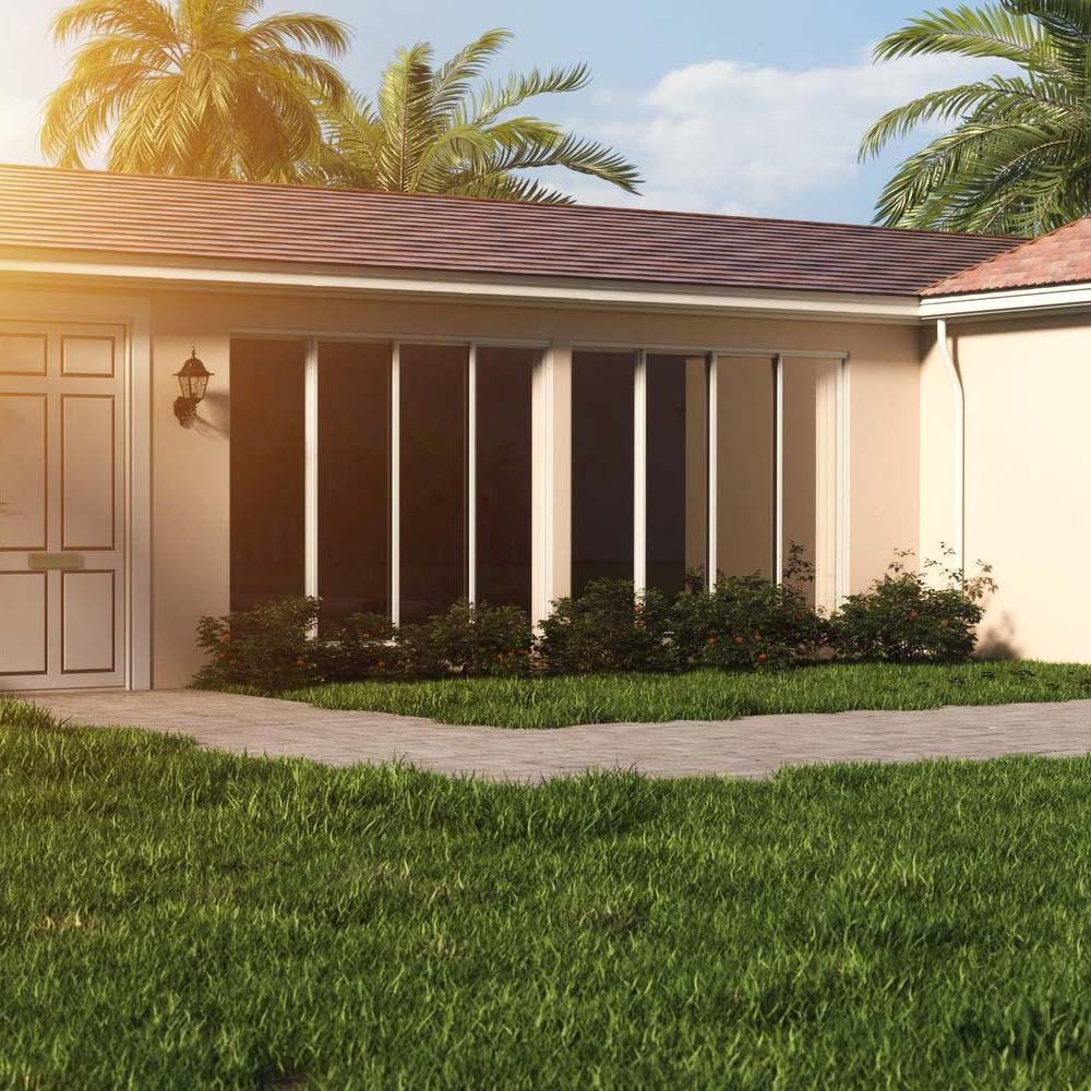 The exterior of a home with a Florida Room with palm trees in the background and a pathway of pavers to the front door. 