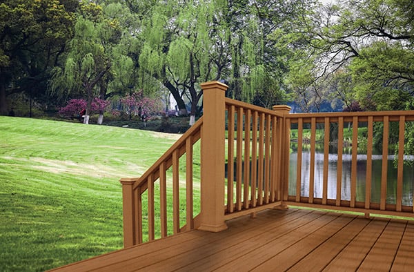 A wooden deck with railing overlooking a pond, green grass, and willow trees. 